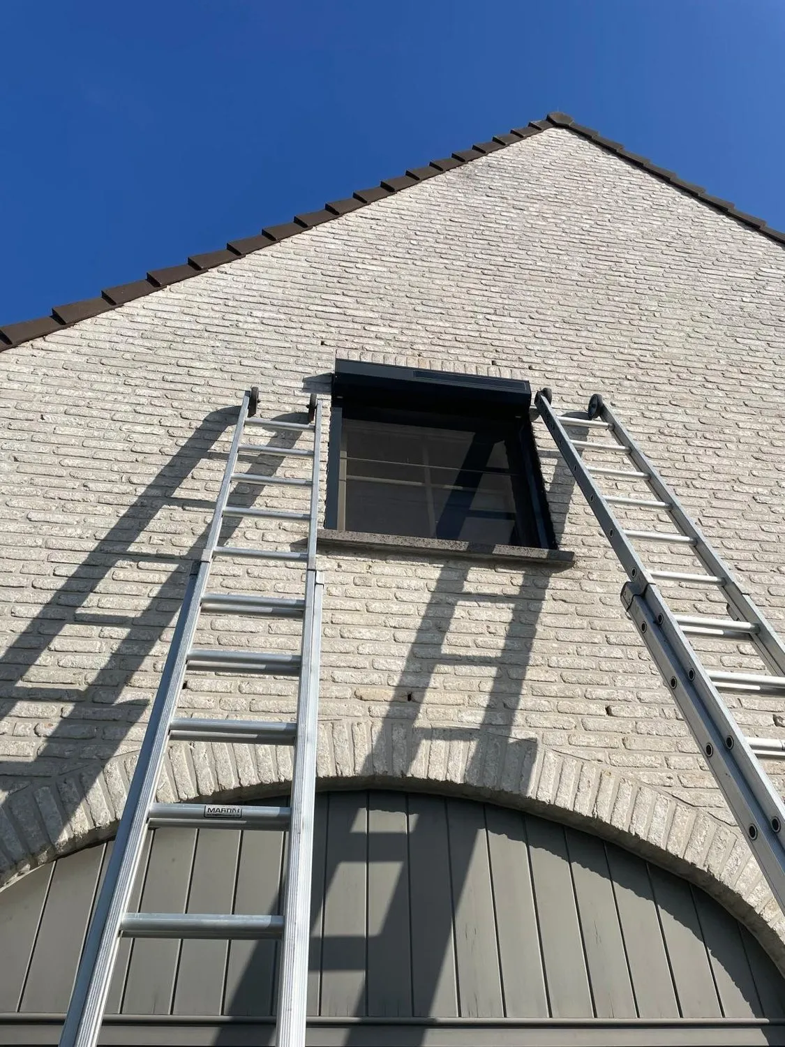 Plaatsing van een rolluik door Atelio, met ladders tegen de gevel.